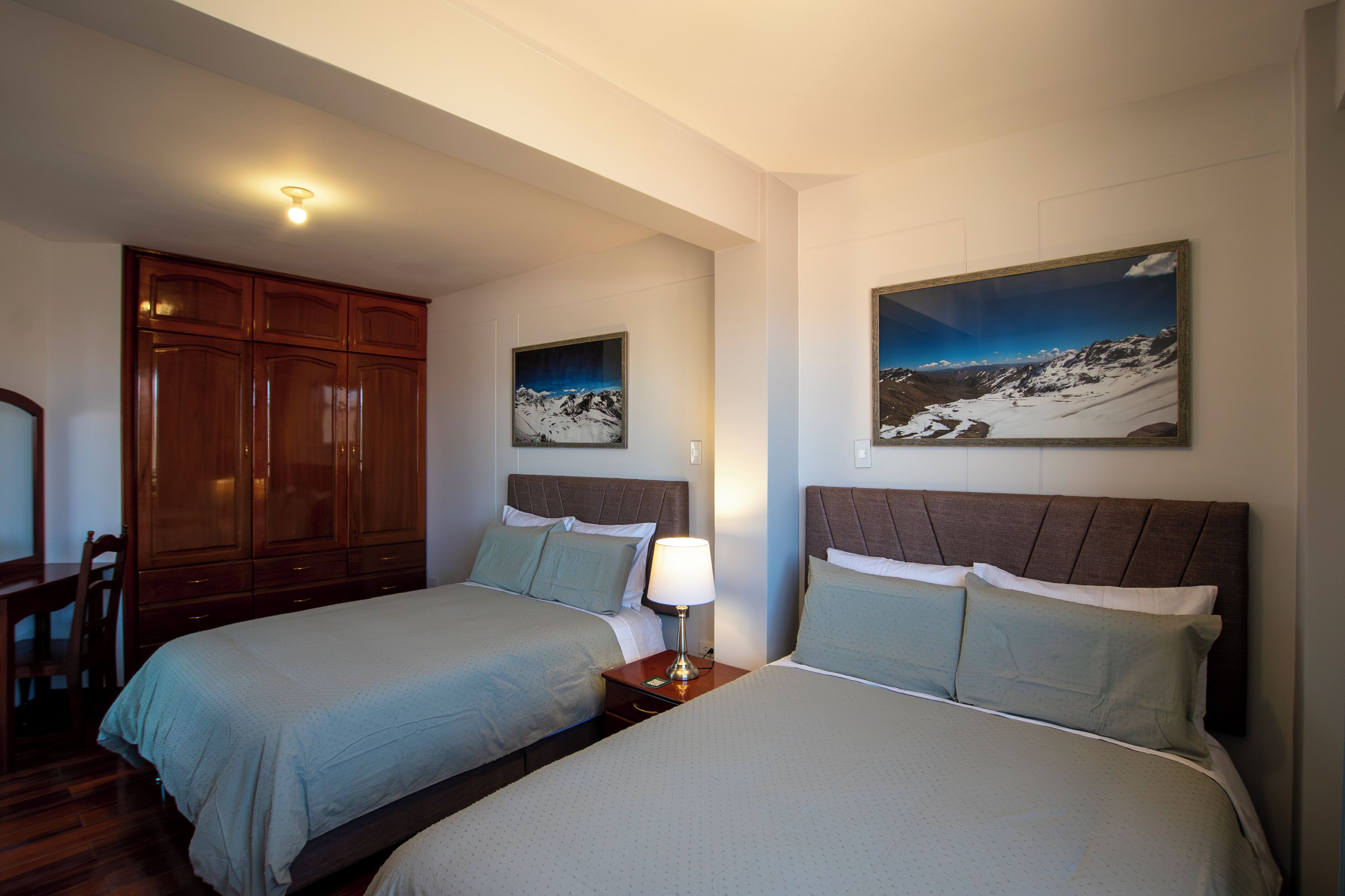 Een hotelkamer met twee bedden, een houten garderobe en twee ingelijste foto's aan de muur.