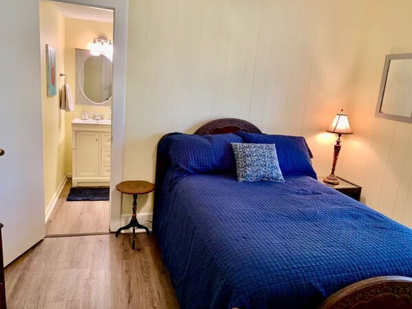 Une chambre à coucher comprenant un lit, une table de chevet, une lampe et une porte donnant sur une salle de bain.