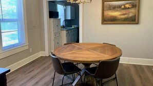 Ein Essbereich mit einem runden Holztisch, vier Stühlen, einer Kandelaberleuchte und einem Bild an der Wand.