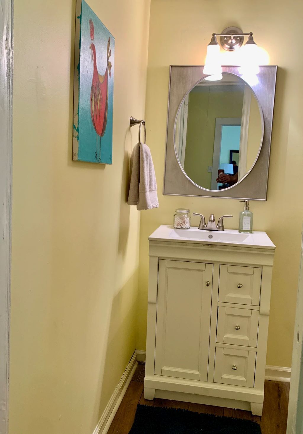 A bathroom with a white vanity, a large mirror, and a painting of a flamingo on the wall.