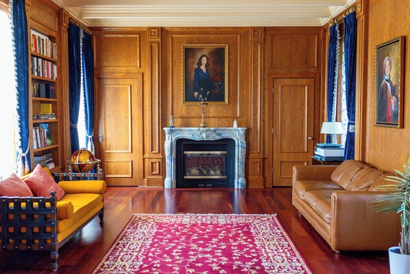 Une pièce avec une cheminée, un canapé jaune, un divan en cuir marron et une bibliothèque.