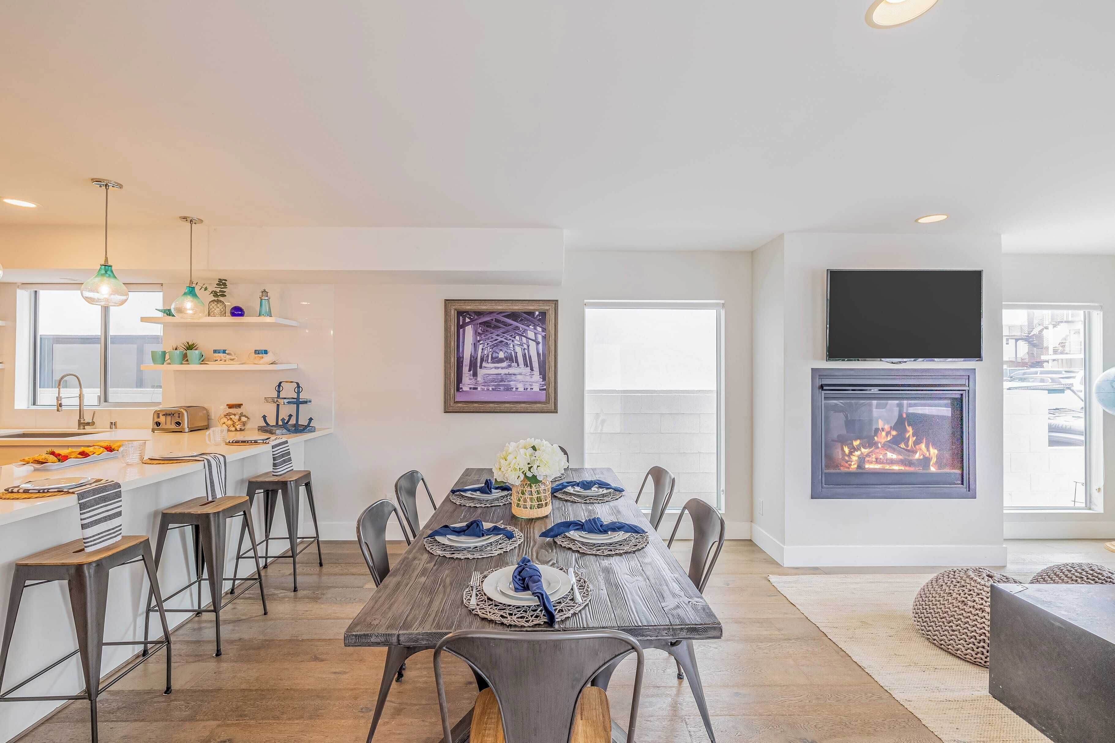Een moderne keuken met een centraal eiland, een eethoek met een houten tafel voor zes personen, en een open haard.