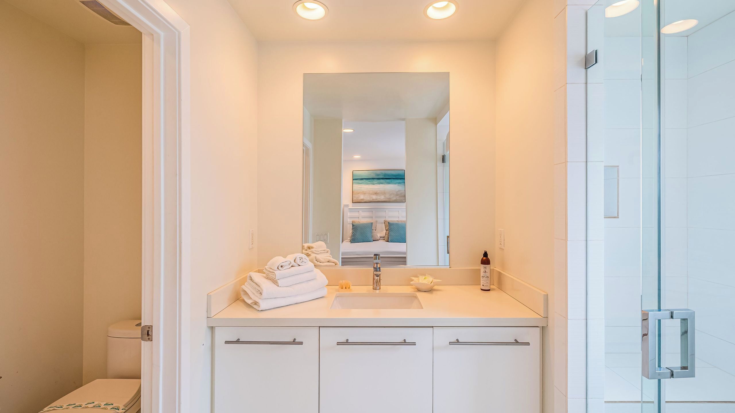 A modern bathroom with a large mirror, a sink, and a glass shower enclosure.