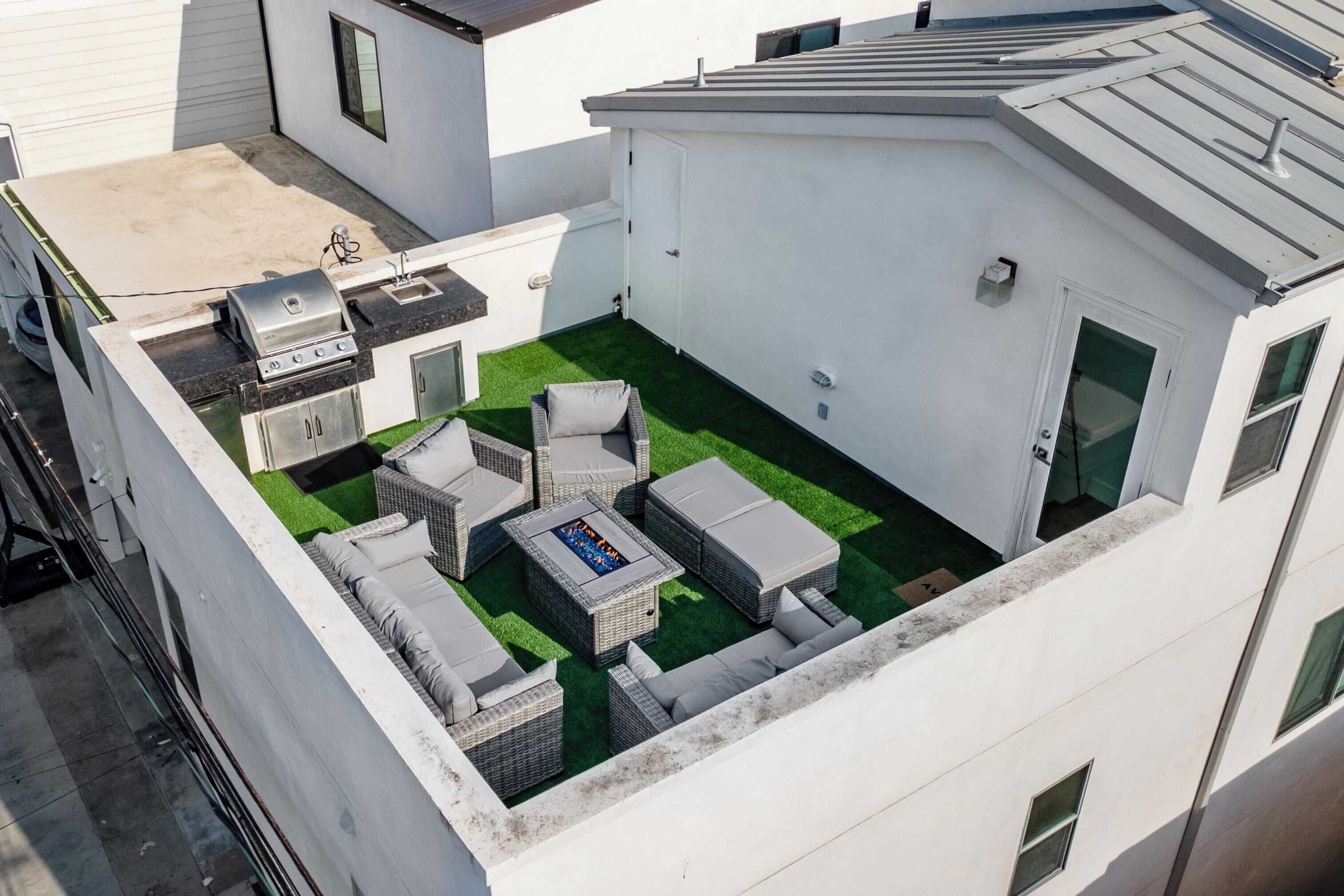 Eine Dachterrasse mit Grill, Gartenmöbeln und einer kleinen Feuerstelle.