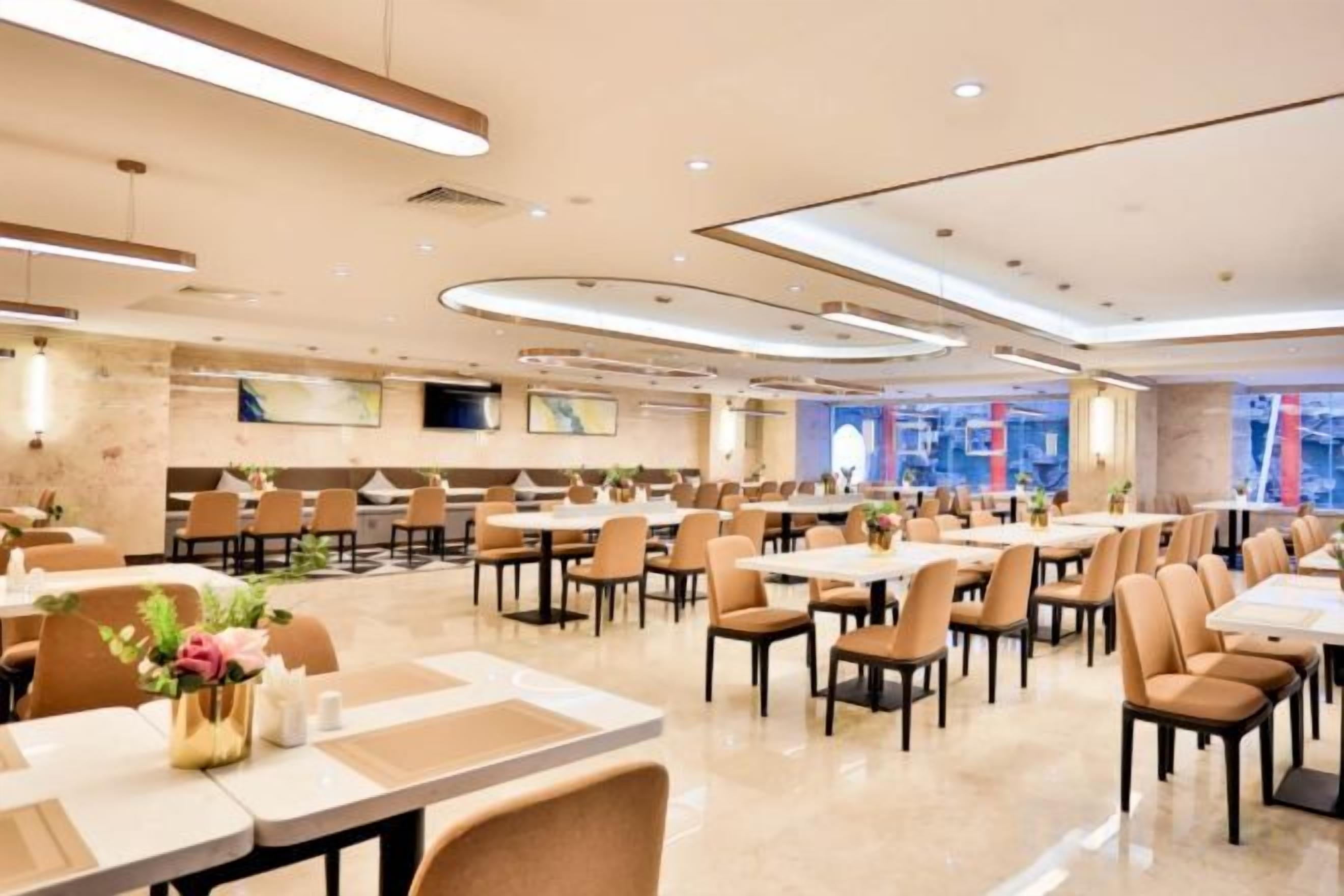 Uma sala de jantar ampla com várias mesas e cadeiras, decoração moderna e clean, e uma grande janela com vista para a cidade.