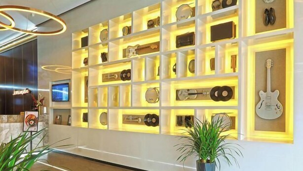 Eine Wand mit mehreren Regalen, auf denen verschiedene Gegenstände, darunter Gitarren und Schallplatten, ausgestellt sind, in einem gut beleuchteten Eingangsbereich.