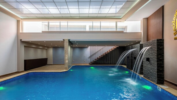 An indoor swimming pool with a modern design, featuring a central water feature and a staircase leading to an upper level. - Stylish apartment with swimming pool, sauna and hammam in central Marrakech   (Marrakech)