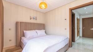 A bedroom with a large bed, a headboard, a wall-mounted light fixture, and a door leading to another room. - Stylish apartment with swimming pool, sauna and hammam in central Marrakech   (Marrakech)