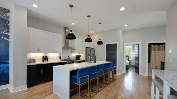 A modern kitchen with white cabinets, a central island with blue bar stools, and pendant lighting.