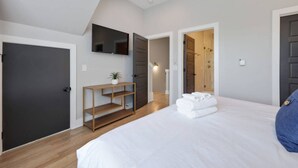 A bedroom with a bed, a TV mounted on the wall, a wooden console table, and a door leading to another room.