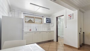 Een moderne keuken met witte kastjes, een magnetron en een raam met jaloezieën.