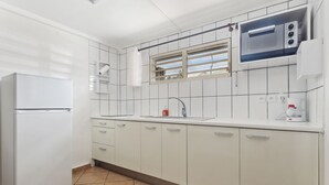 Een moderne keuken met witte kastjes, een inbouwmagnetron en een raam met jaloezieën.