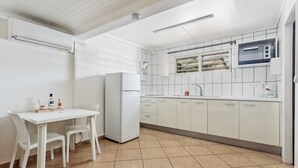 Een kleine keuken met witte kastjes, een inbouwoven en een eethoekje met een witte tafel en stoelen.