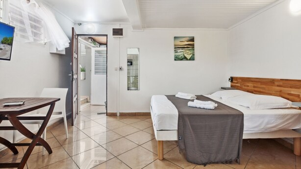 A hotel room with a bed, a small table, a bench, a mirror, and a painting on the wall. - Studio 1-Anthurium - A 7min de la plage (Les Trois-Îlets)