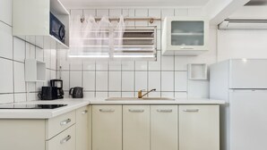 A modern kitchen with white cabinets, a built-in oven, a microwave, and a coffee maker. - Studio 1-Anthurium - A 7min de la plage (Les Trois-Îlets)