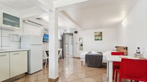 A modern hotel room with a kitchenette, a dining area with red chairs, a bed with a gray bedspread, and a painting on the wall. - Studio 1-Anthurium - A 7min de la plage (Les Trois-Îlets)