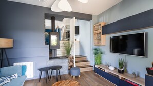 A modern living room with a sofa, coffee table, and TV. There are stairs leading to a kitchen and a staircase. - La Petite Mouette - Maison au port de Dahouët (Pléneuf-Val-André)