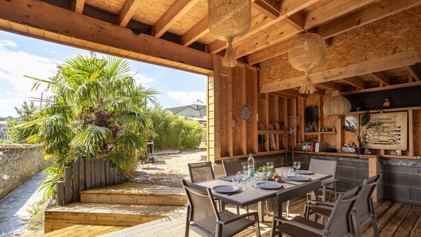 An outdoor dining area with wooden tables and chairs, surrounded by plants and a wooden deck. - La Petite Mouette - Maison au port de Dahouët (Pléneuf-Val-André)