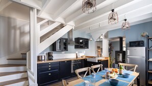 A modern kitchen with dark cabinets, a wooden staircase, and a dining area with blue placemats. - La Petite Mouette - Maison au port de Dahouët (Pléneuf-Val-André)