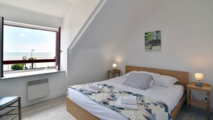 A bedroom with a large window, a bed with a quilt, two bedside tables with lamps, and a small plant on the windowsill.