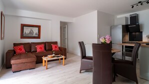 Un salon moderne avec un canapé marron, une table basse et un coin repas comprenant une chaise et une table. Il y a aussi une cuisine équipée d’une cuisinière et d’un réfrigérateur.