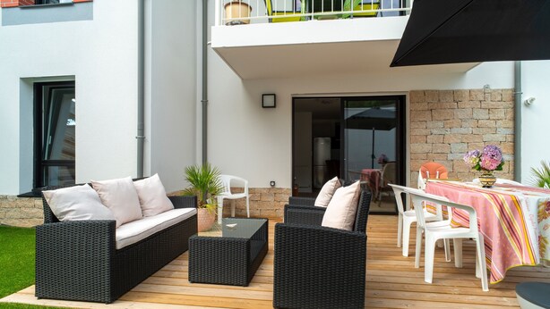 Une terrasse extérieure avec des meubles en osier, une table recouverte d’une nappe à rayures et des plantes en pot.