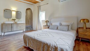 Ein Schlafzimmer mit einem großen Bett, einem Holzkopfteil, Nachttischen mit Lampen, einer Kommode und einem Spiegel.