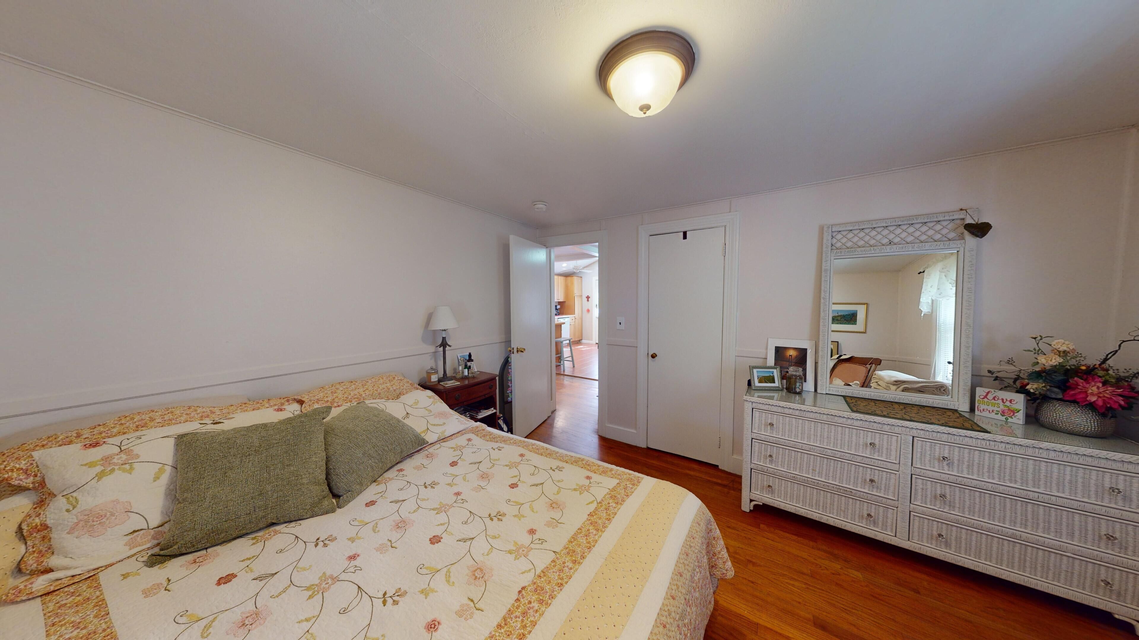 A bedroom with a bed, dresser, mirror, and a hallway leading to a bathroom.