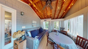 A cozy room with a wooden ceiling, a grey sofa, a table with a checkered tablecloth, and a window with curtains. - "Charming 2-Bedroom Home in Narragansett with Private Beach Access and WiFi" (Narragansett)
