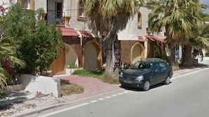 A building with arched windows and a red-tiled roof, parked cars, and palm trees. - Dar Lella (Bizerte)