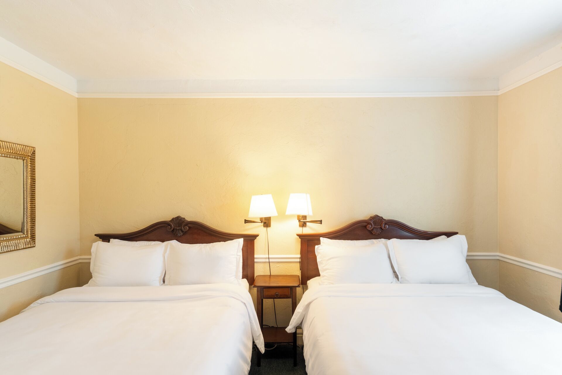 A hotel room with two beds, a nightstand, and two wall-mounted lamps.