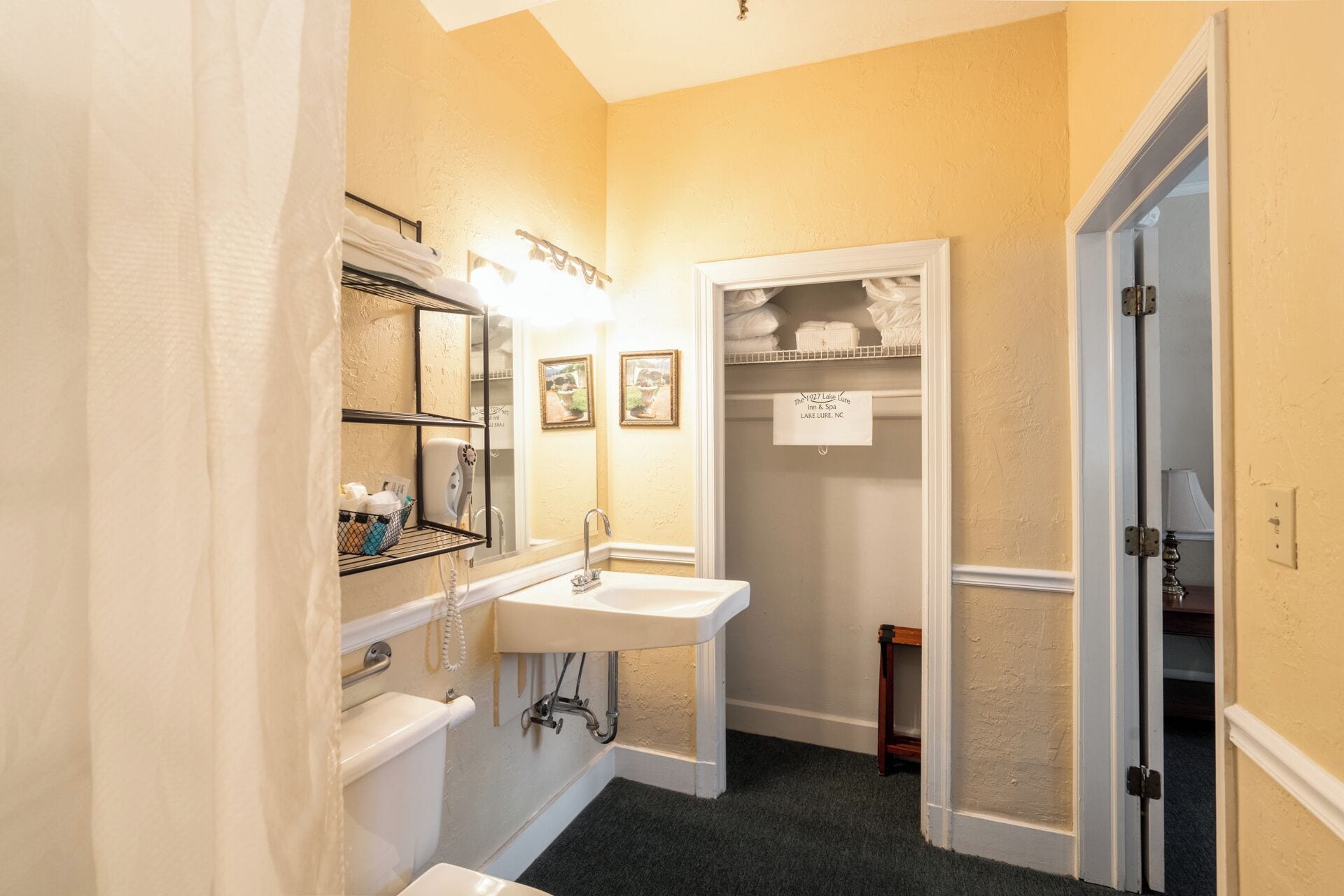 A bathroom with a sink, toilet, and towel rack. There is a door leading to a closet with shelves.