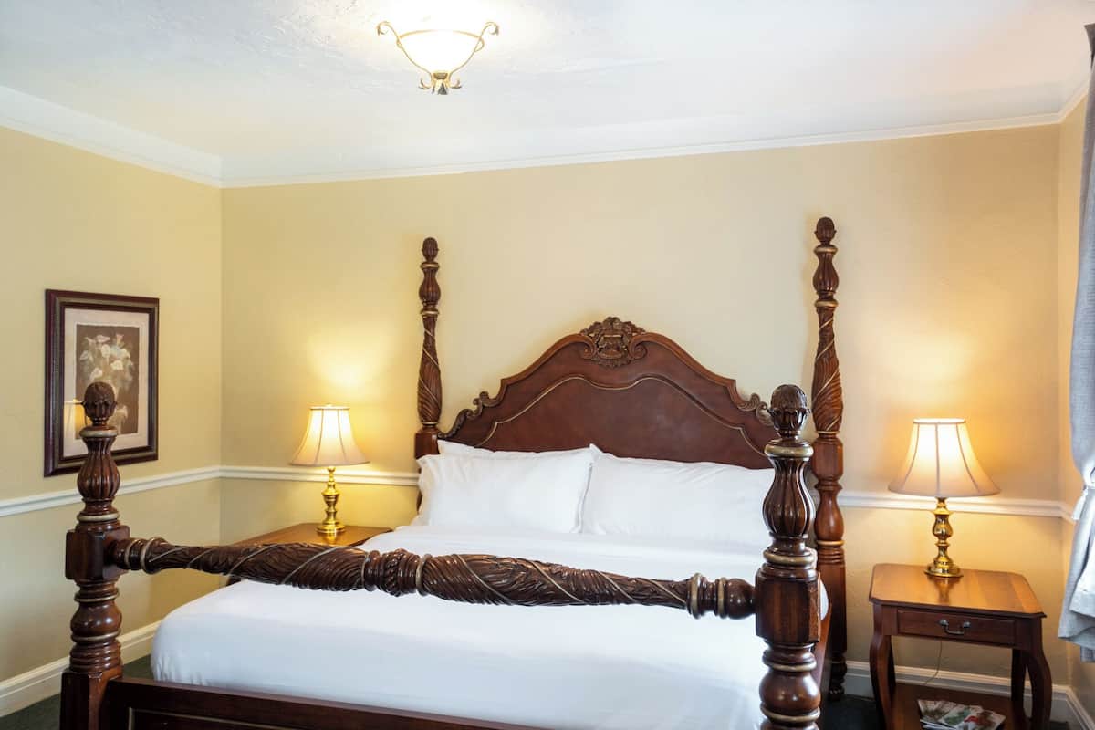 A four-poster bed with a wooden headboard, two bedside lamps, and a framed picture on the wall.