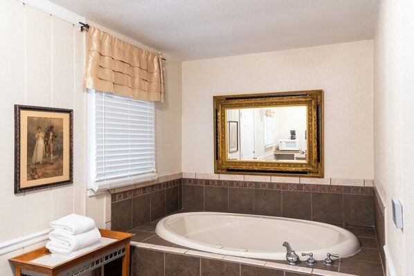 A bathroom with a bathtub, a framed mirror, a window with blinds, and a framed picture on the wall. - Lake Lure Inn & Spa (Lake Lure)