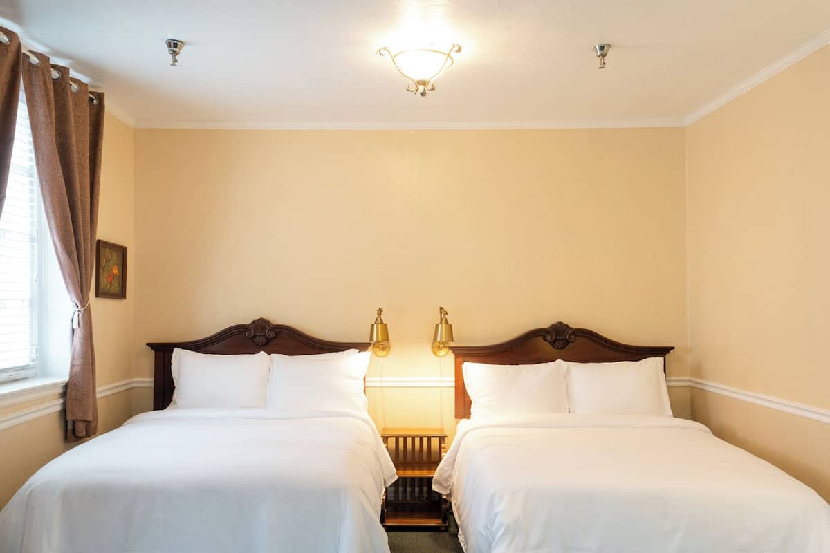 A hotel room with two single beds, a nightstand, a small table, and a ceiling light fixture.