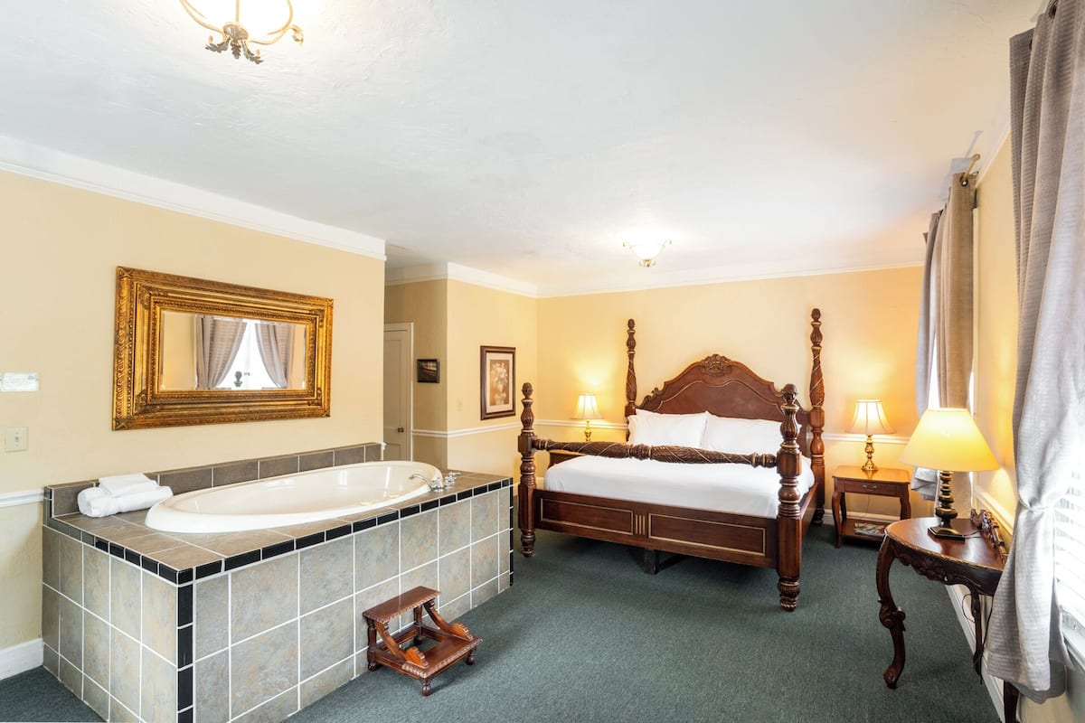 A hotel room with a large bed, a bathtub, and a vanity with a mirror.