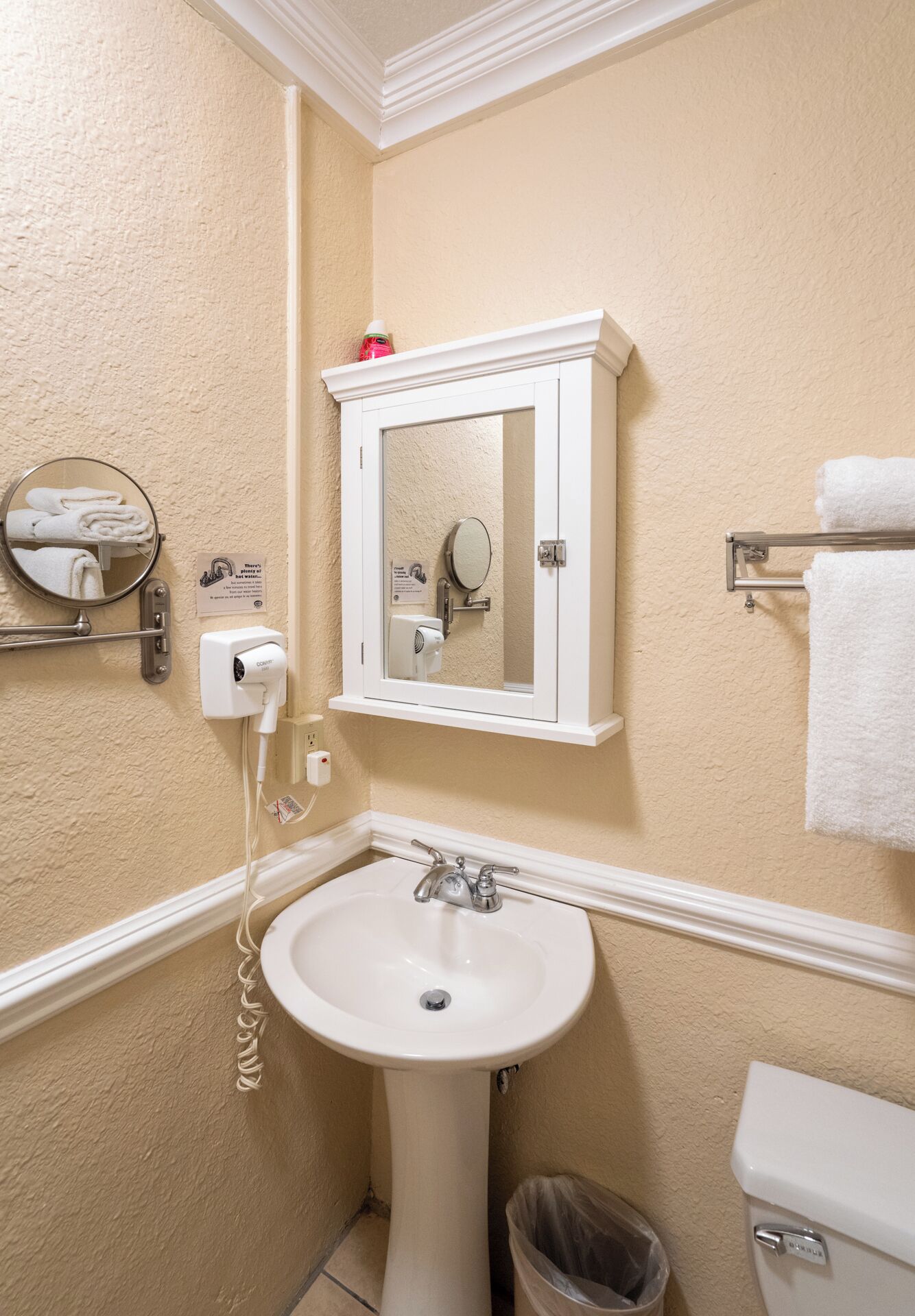 A bathroom with a pedestal sink, a mirror cabinet, a towel rack, and a toilet.