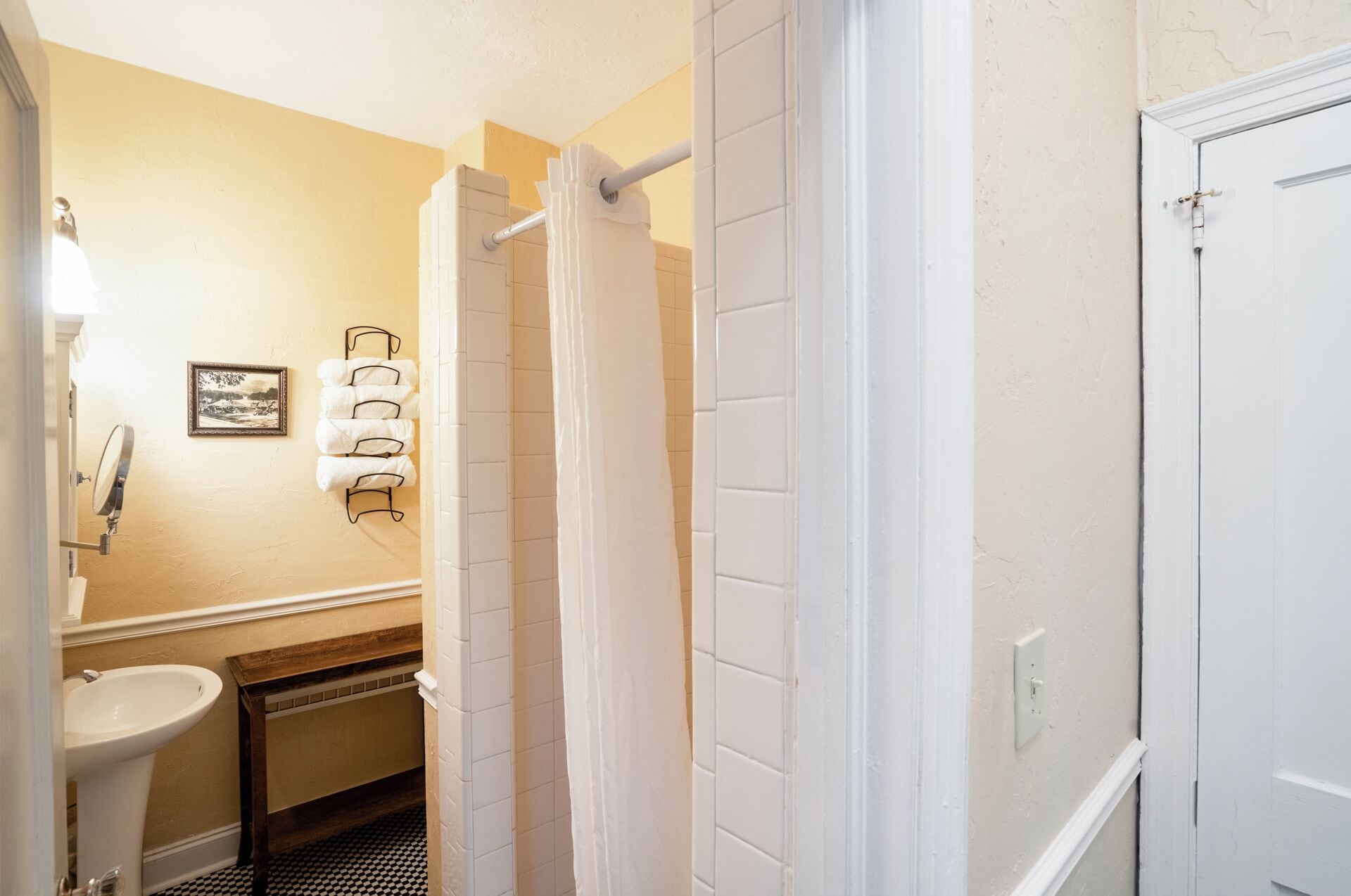 Een badkamer met een witte wastafel, een spiegel, een handdoekrek met handdoeken, een douchegordijn en een deur.