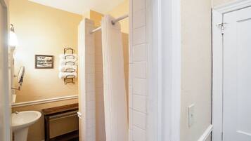 A bathroom with a white sink, a mirror, a towel rack with towels, a shower curtain, and a door.