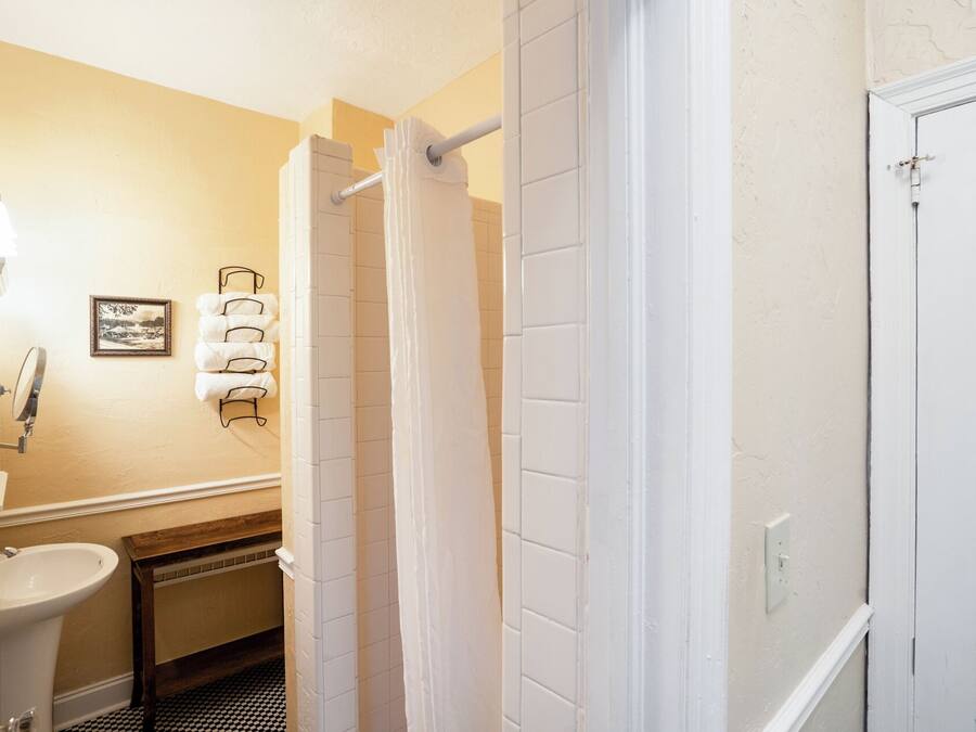 A bathroom with a white sink, a mirror, a towel rack with towels, a shower curtain, and a door.