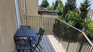 A wooden deck with a table and chairs, a metal railing, and a beige wall. - Le P'tit Colin 1er (Pontarlier)