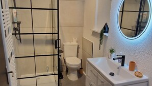 A modern bathroom with a glass shower enclosure, a toilet, a sink with a mirror, and a built-in washing machine. - Le P'tit Colin 1er (Pontarlier)
