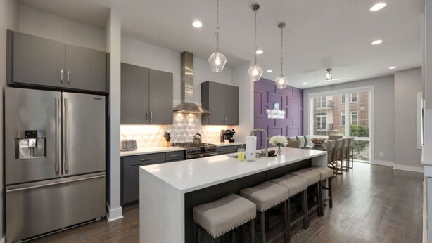 A modern kitchen with a large island, stainless steel appliances, pendant lighting, and a view to the outside. - Walk to West End | Rooftop Terrace + Deck (Nashville)