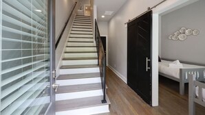 A staircase with a modern design, a black door, and a bed with white bedding. - Walk to West End | Rooftop Terrace + Deck (Nashville)