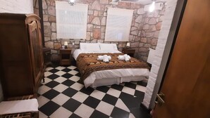 Une pièce avec un sol à carreaux, un lit recouvert d’une couverture à motifs, une armoire en bois et des murs en pierre.
