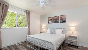 A bedroom with a bed, two bedside tables, a ceiling fan, a window with curtains, and wall-mounted artwork. - 2 Condos, Minutes From Downtown, Parks, and Freeway! (Boise)