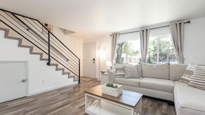 A living room with a staircase, a sofa, a coffee table, and a door. - 2 Condos, Minutes From Downtown, Parks, and Freeway! (Boise)