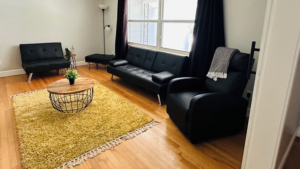 A living room with a black sofa, a small coffee table, and a yellow rug.