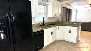 A kitchen with white cabinets, a black refrigerator, and a granite countertop.