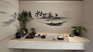 A room with a minimalist design, featuring a low wooden desk with various items, a large wall mural, and potted plants. - Jiajie Boutique Hotel (Lingao Cultural Park Fulo Plaza Branch) (Lingao)